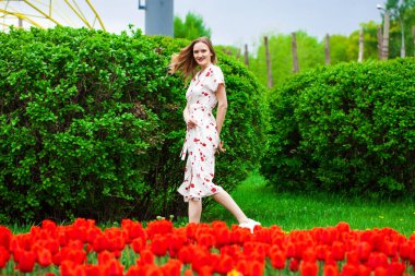 Kırmızı lalelerin arka planında poz veren güzel sarışın bir kadının vücut portresi.