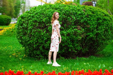 Kırmızı lalelerin arka planında poz veren güzel sarışın bir kadının vücut portresi.