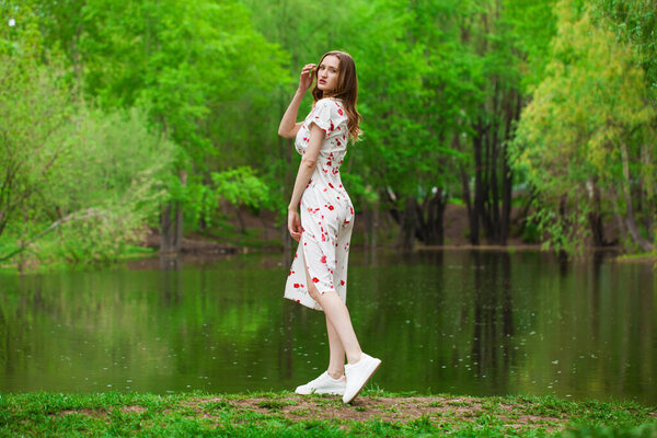 Full body portrait of a young beautiful woman in white dress posing by the lake