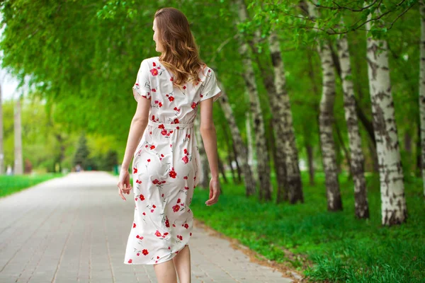 一个年轻美丽的金发女子穿着白花衣服走在春天大街上的画像 — 图库照片