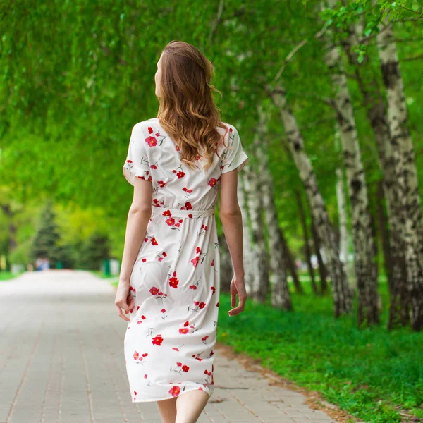 一个年轻美丽的金发女子穿着白花衣服走在春天大街上的画像 — 图库照片