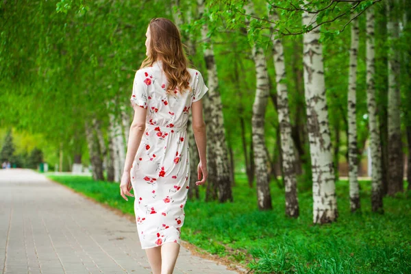 一个年轻美丽的金发女子穿着白花衣服走在春天大街上的画像 — 图库照片