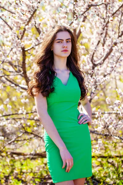 白い花と桜の木の近くにポーズを緑のドレスの美しさ10代の女の子 春の公園 — ストック写真