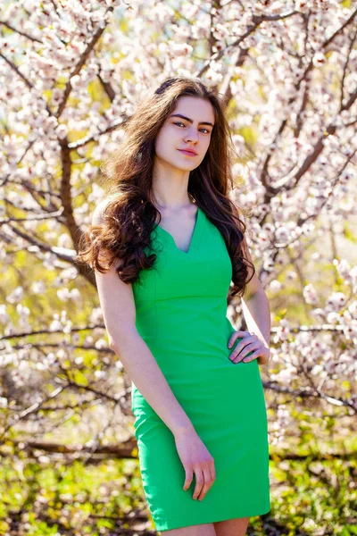 白い花と桜の木の近くにポーズを緑のドレスの美しさ10代の女の子 春の公園 — ストック写真