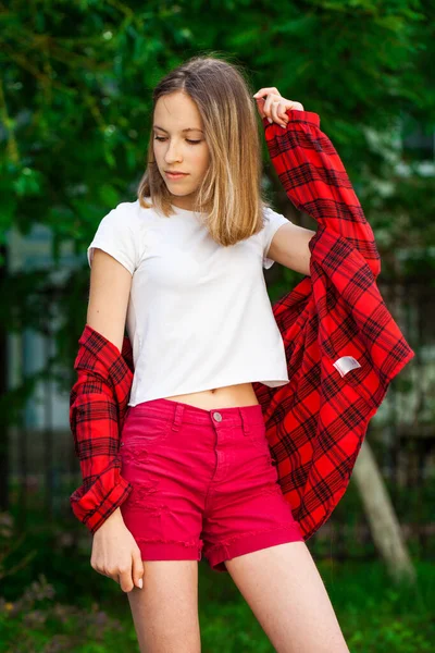 一个身穿白色T恤和红色牛仔裤短裤的年轻漂亮金发姑娘的画像 夏季公园室外背景 — 图库照片
