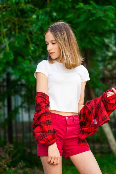 一个身穿白色T恤和红色牛仔裤短裤的年轻漂亮金发姑娘的画像 夏季公园室外背景 — 图库照片