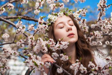 Güzel genç kız çiçek açan kiraz ağacının yanında beyaz çiçeklerle poz veriyor. Bahar geldi. 