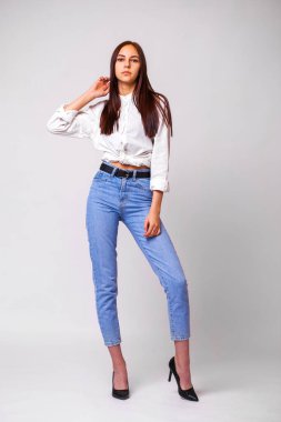 Kot pantolonlu güzel, seksi esmer kadın. Kot pantolon giymiş bir manken. Gri stüdyo arka planında izole edilmiş.