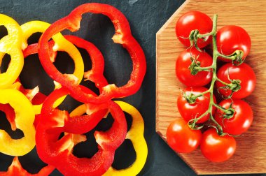 Taze biber halkaları dalı kesme tahtası ve koyu mavi arka plan üzerinde kırmızı domates ile