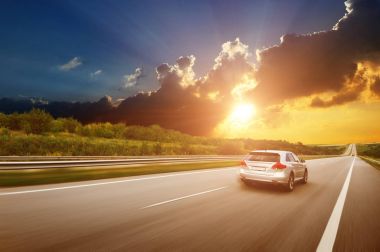 Gece gökyüzünde bulutlar ve güzel bir gün batımı ile karşı kırsal asfalt yol üzerinde hızlı araba gümüş crossover araba
