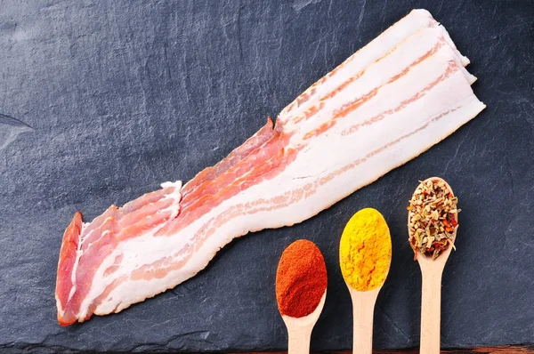 Raw Bacon Slices Wooden Spoons Dry Spices Slate Slab — Stock Photo, Image