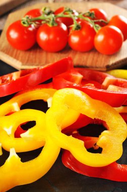 Taze biber halkaları dalı kesme tahtası ve koyu mavi arka plan üzerinde kırmızı domates ile