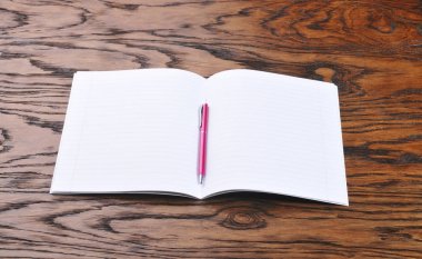 Koyu kahverengi ahşap arka plan üzerinde pembe kalem ile okul defterini açıldı