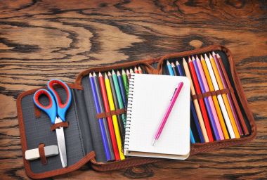 Renkli kalemler dolu mavi makas, defter, silgi ve kahverengi ahşap masa üzerinde pembe bir kalem kalem
