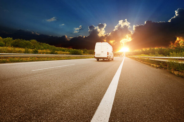 Big white van on the countryside road shipping goods against night sky with sunset