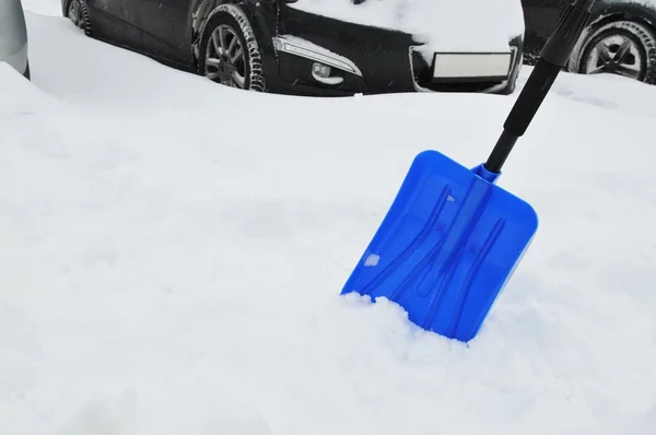 蓝色铁锹在雪反对汽车在停车 — 图库照片