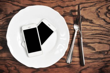 İki plaka üzerinde siyah ekranlı akıllı telefonlar ile gümüş bıçak ve çatal ahşap arka plan üzerinde beyaz