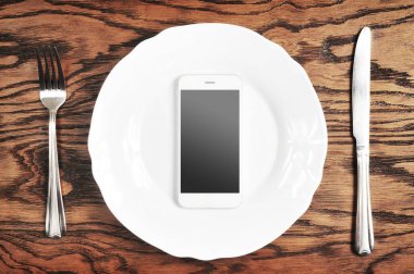 Gümüş bıçak ile plaka üzerinde siyah ekran ve çatal ahşap arka plan üzerinde beyaz smartphone