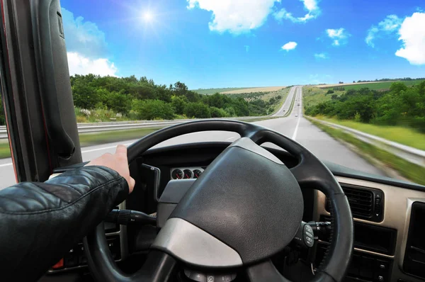 ドライバーとトラックのダッシュ ボードに対して太陽と青い空の田舎道のステアリング ホイールに手します — ストック写真