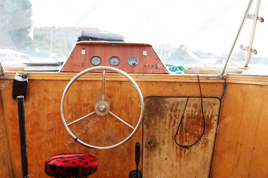 Wooden control panel with metal steering wheel on the captain bridge of the old motor boat