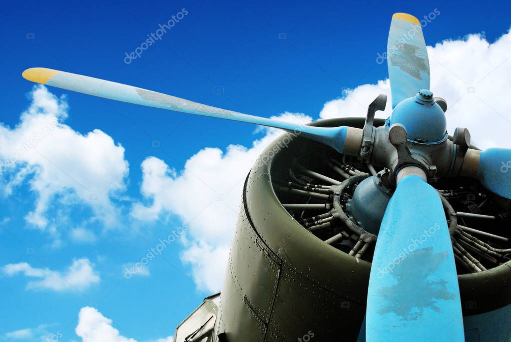 Old green plane engine with blue and yellow propeller against blue sky with clouds