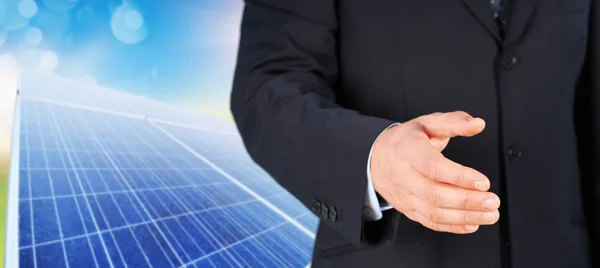 Closeup of a businessman in black suit giving hand for handshake with solar panels on background