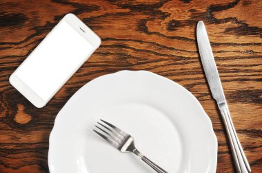 boş ekran ve plaka ile gümüş bıçak ve çatal ahşap arka plan üzerinde beyaz smartphone