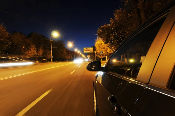 Black car driving fast on the road in the dark night city with lights