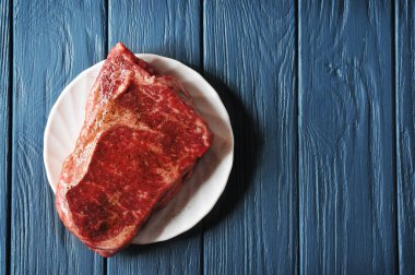 Çiğ et biftek koyu mavi ahşap arka plan üzerinde beyaz bir tabakta parçası