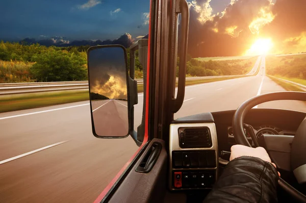 ステアリング ホイール上のドライバー手と側バックミラーの夕日と夜空に対して田舎道 トラックのダッシュ ボード ロイヤリティフリーのストック画像