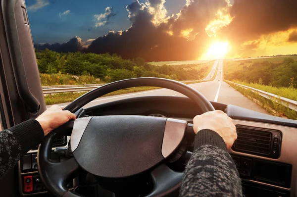 Truck dashboard with driver\'s hand on the steering wheel on the countryside road against night sky with sunset