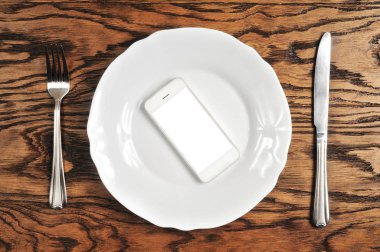 Beyaz perdeye sahip olan gümüş tabakta ve koyu ahşap arka plan üzerinde çatalı ile beyaz smartphone