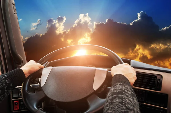 Truck dashboard with drivers hands on the steering wheel against night sky with sunset