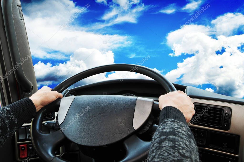 Truck dashboard with driver hands on the steering wheel against sky with clouds
