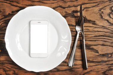 Beyaz perdeye sahip olan gümüş tabakta ve koyu ahşap arka plan üzerinde çatalı ile beyaz smartphone