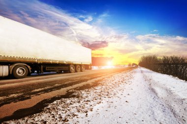 Beyaz kamyon ve kar mavi gökyüzü bulutlar ve parlak günbatımı karşı olan kış kırsal yol üzerinde metin için yer ile beyaz bir römork