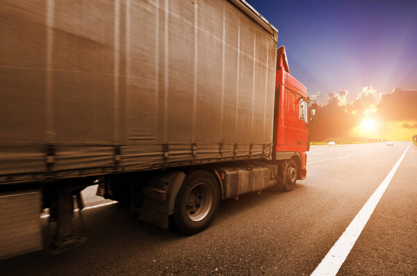 Red truck with the grey trailer on the countryside road against a night sky with a beutiful sunset