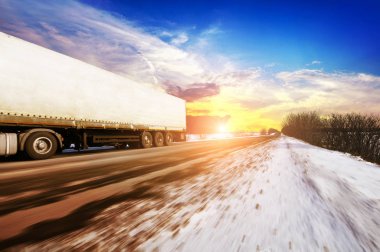 Beyaz kamyon ve hızlı yolda kış kırsal mavi gökyüzü bulutlar ve parlak günbatımı karşı kar ile sürüş metin için yer ile beyaz bir römork