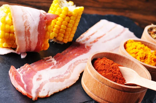 Bacon skivor och trä skålar med torra kryddor på Mörk blå b — Stockfoto