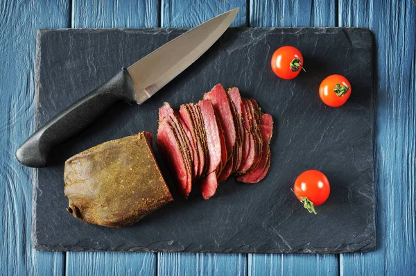 Нарізане м'ясо, ніж і помідори на темній дошці і дерев'яний синій — стокове фото