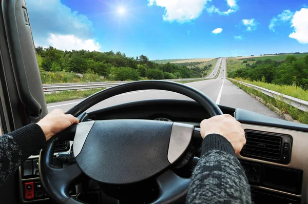 Truck dashboard with driver hands on the steering wheel on the countryside road against blue sky with sun