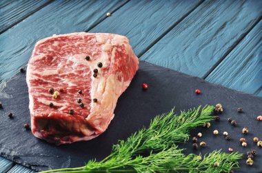 Yeşil dereotu ve karabiber bir kesme tahtası ve mavi ahşap arka plan avuç çiğ et biftek