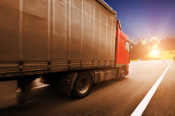 Red truck driving fast with the grey trailer on the countryside road against a night sky with a beutiful sunset