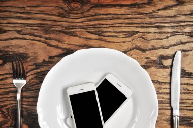 İki plaka üzerinde büyük siyah ekranlı akıllı telefonlar ile gümüş bıçak ve çatal koyu ahşap arka plan üzerinde beyaz