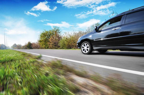 Schwarzes Familienauto Rast Auf Landstraße Mit Grünen Bäumen Gegen Blauen Stockbild