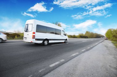 White van and other cars on the countryside asphalt road against blue sky with clouds