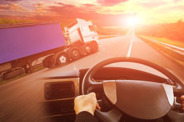 Abstract background with truck with trailer, truck steering wheel and road against sky with sunset
