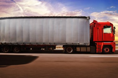 Red truck and white trailer with space for text driving fast on the countryside road against sky with sunset