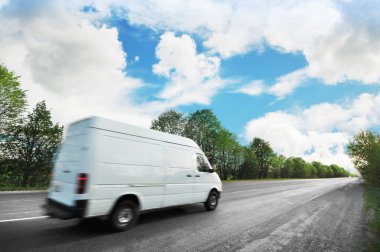 Big white van on the countryside road shipping goods against blue sky with clouds