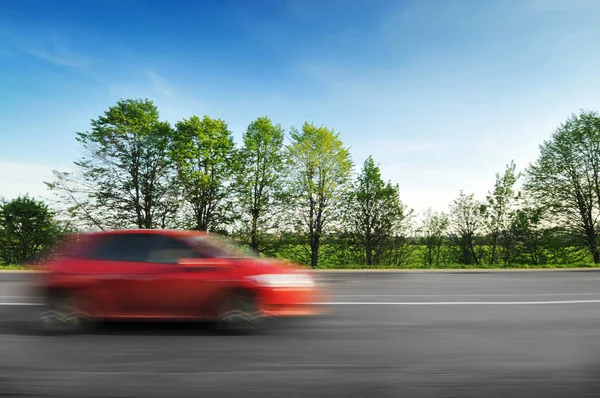 一辆红色的背靠背汽车在乡间路上疾驰而过 绿树成荫 灌木丛映衬着蓝天 免版税图库图片
